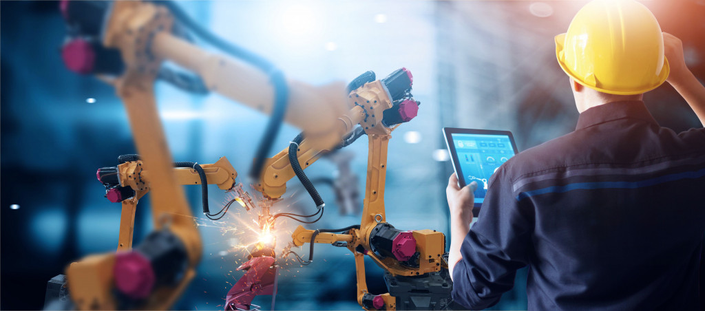 Robotic arms being controlled by a person wearing a hard hat for welding