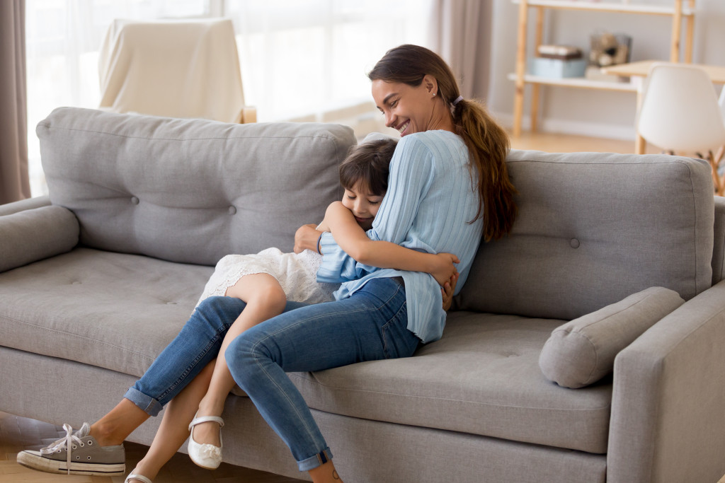 A mother and daughter hugging each other while sitting on a couch at home.