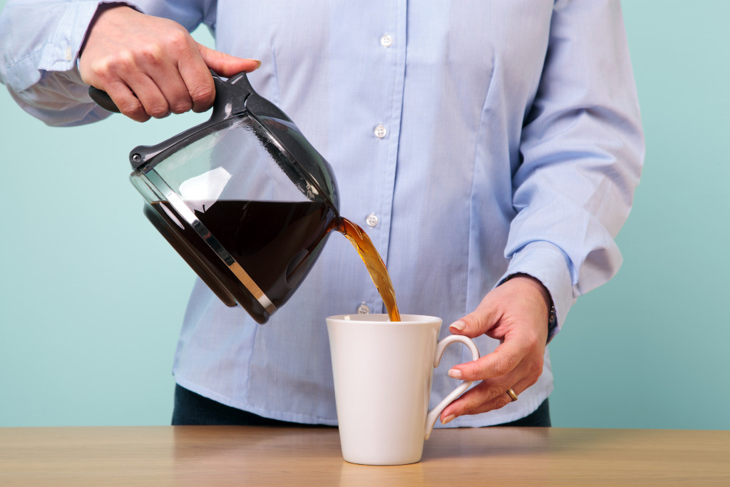A person pouring coffee from a glass pot to a mug